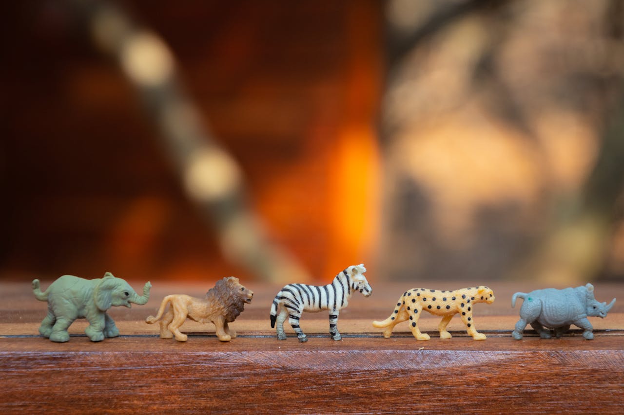 Miniature toy animals in a row on wood, displaying various wild species.