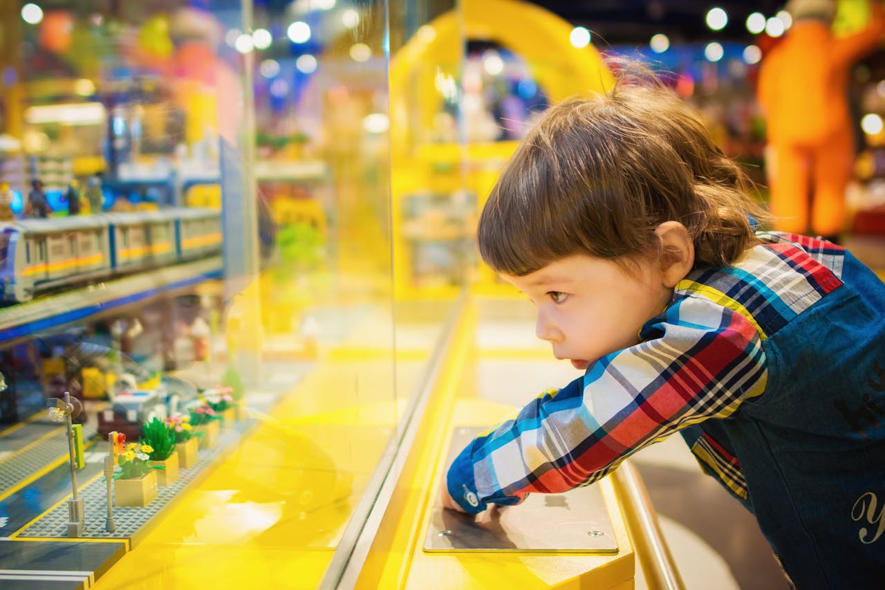 A young boy intently observes a colorful toy train display in a vibrant toy store.