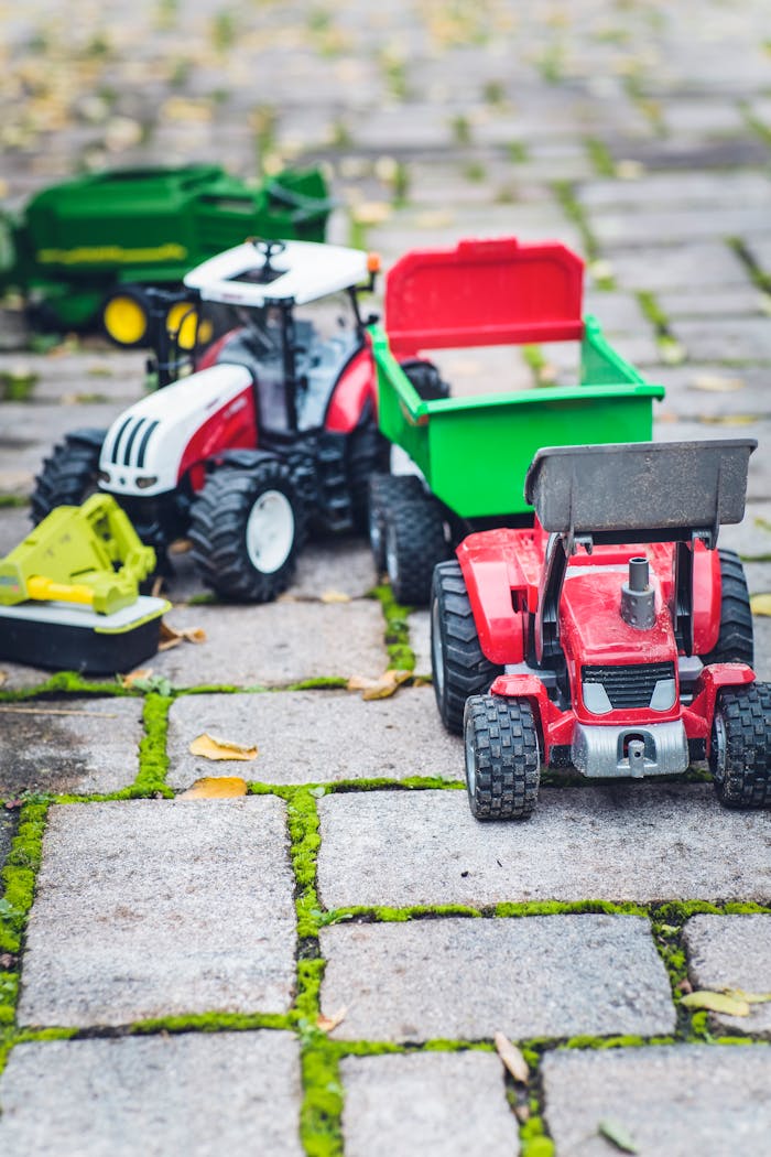 Colorful toy tractors and farming equipment on an outdoor cobblestone path.